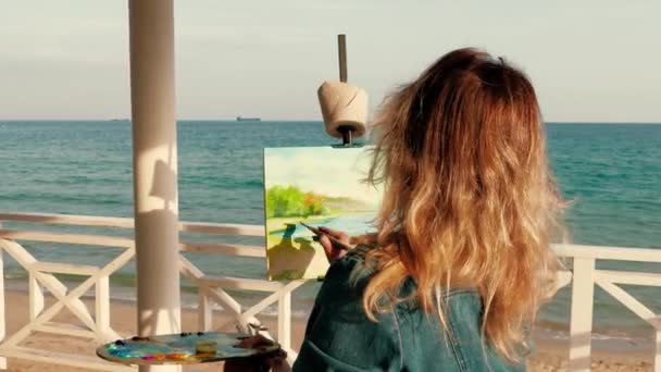Młoda kobieta artysta malarstwo seascape stojąc na tarasie przy plaży drewniane — Wideo stockowe