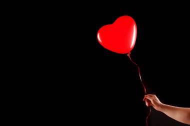 Kadın eli kırmızı kauçuk, şişme kalp şeklinde balon tutuyor. Aşk, ilişki, sevgililer günü ve doğum günü kutlaması konsepti. Stüdyo görüntüsü boş kopya alanı olan bulanık bir arkaplan üzerinde