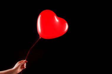 Kadın eli kırmızı kauçuk, şişme kalp şeklinde balon tutuyor. Aşk, ilişki, sevgililer günü ve doğum günü kutlaması konsepti. Stüdyo görüntüsü boş kopya alanı olan bulanık bir arkaplan üzerinde