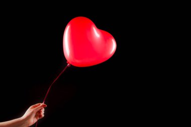 Kadın eli kırmızı kauçuk, şişme kalp şeklinde balon tutuyor. Aşk, ilişki, sevgililer günü ve doğum günü kutlaması konsepti. Stüdyo görüntüsü boş kopya alanı olan bulanık bir arkaplan üzerinde