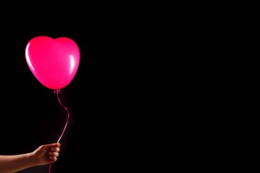 Kadın eli kırmızı kauçuk, şişme kalp şeklinde balon tutuyor. Aşk, ilişki, sevgililer günü ve doğum günü kutlaması konsepti. Stüdyo görüntüsü boş kopya alanı olan bulanık bir arkaplan üzerinde