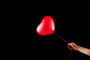 Kadın eli kırmızı kauçuk, şişme kalp şeklinde balon tutuyor. Aşk, ilişki, sevgililer günü ve doğum günü kutlaması konsepti. Stüdyo görüntüsü boş kopya alanı olan bulanık bir arkaplan üzerinde