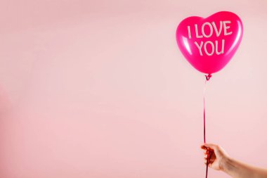 Kadın eli kırmızı kauçuk, şişme kalp şeklinde balon tutuyor. Aşk, ilişki, sevgililer günü ve doğum günü kutlaması konsepti. Stüdyo görüntüsü boş kopya alanı olan bulanık bir arkaplan üzerinde