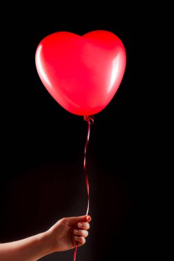 Kadın eli kırmızı kauçuk, şişme kalp şeklinde balon tutuyor. Aşk, ilişki, sevgililer günü ve doğum günü kutlaması konsepti. Stüdyo görüntüsü boş kopya alanı olan bulanık bir arkaplan üzerinde