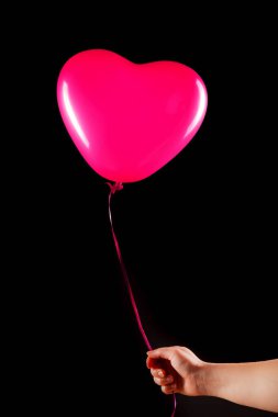 Kadın eli kırmızı kauçuk, şişme kalp şeklinde balon tutuyor. Aşk, ilişki, sevgililer günü ve doğum günü kutlaması konsepti. Stüdyo görüntüsü boş kopya alanı olan bulanık bir arkaplan üzerinde