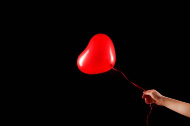Kadın eli kırmızı kauçuk, şişme kalp şeklinde balon tutuyor. Aşk, ilişki, sevgililer günü ve doğum günü kutlaması konsepti. Stüdyo görüntüsü boş kopya alanı olan bulanık bir arkaplan üzerinde