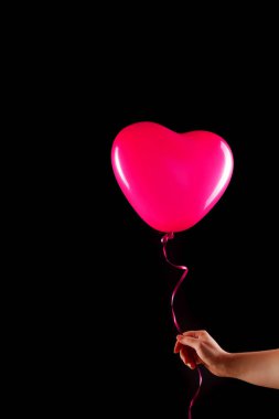 Kadın eli kırmızı kauçuk, şişme kalp şeklinde balon tutuyor. Aşk, ilişki, sevgililer günü ve doğum günü kutlaması konsepti. Stüdyo görüntüsü boş kopya alanı olan bulanık bir arkaplan üzerinde