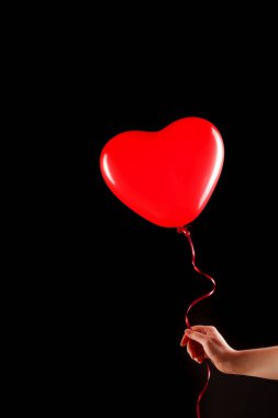 Kadın eli kırmızı kauçuk, şişme kalp şeklinde balon tutuyor. Aşk, ilişki, sevgililer günü ve doğum günü kutlaması konsepti. Stüdyo görüntüsü boş kopya alanı olan bulanık bir arkaplan üzerinde