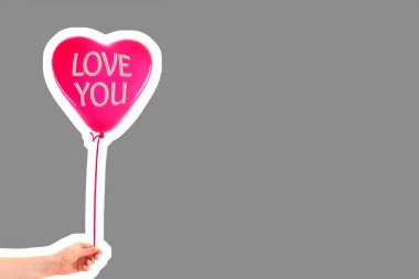 Kadın eli kırmızı kauçuk, şişme kalp şeklinde balon tutuyor. Aşk, ilişki, sevgililer günü ve doğum günü kutlaması konsepti. Boş kopya alanı olan dergi tarzı moda kolajı