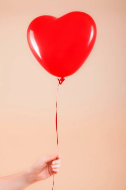 Kadın eli kırmızı kauçuk, şişme kalp şeklinde balon tutuyor. Aşk, ilişki, sevgililer günü ve doğum günü kutlaması konsepti. Stüdyo görüntüsü boş kopya alanı olan bulanık bir arkaplan üzerinde