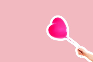 Kadın eli pembe kauçuk, şişme kalp şeklinde balon tutuyor. Aşk, ilişki, sevgililer günü ve doğum günü kutlaması konsepti. Boş kopya alanı olan dergi tarzı moda kolajı