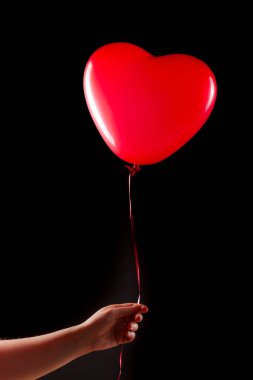 Kadın eli kırmızı kauçuk, şişme kalp şeklinde balon tutuyor. Aşk, ilişki, sevgililer günü ve doğum günü kutlaması konsepti. Stüdyo görüntüsü boş kopya alanı olan bulanık bir arkaplan üzerinde