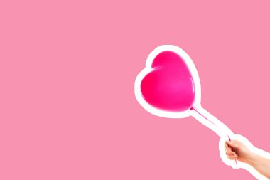Kadın eli pembe kauçuk, şişme kalp şeklinde balon tutuyor. Aşk, ilişki, sevgililer günü ve doğum günü kutlaması konsepti. Boş kopya alanı olan dergi tarzı moda kolajı