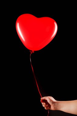 Kadın eli kırmızı kauçuk, şişme kalp şeklinde balon tutuyor. Aşk, ilişki, sevgililer günü ve doğum günü kutlaması konsepti. Stüdyo görüntüsü boş kopya alanı olan bulanık bir arkaplan üzerinde