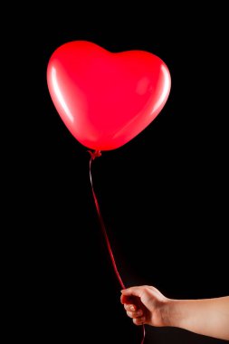 Kadın eli kırmızı kauçuk, şişme kalp şeklinde balon tutuyor. Aşk, ilişki, sevgililer günü ve doğum günü kutlaması konsepti. Stüdyo görüntüsü boş kopya alanı olan bulanık bir arkaplan üzerinde