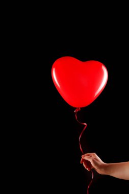 Kadın eli kırmızı kauçuk, şişme kalp şeklinde balon tutuyor. Aşk, ilişki, sevgililer günü ve doğum günü kutlaması konsepti. Stüdyo görüntüsü boş kopya alanı olan bulanık bir arkaplan üzerinde
