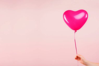 Kadın eli pembe kauçuk, şişme kalp şeklinde balon tutuyor. Aşk, ilişki, sevgililer günü ve doğum günü kutlaması konsepti. Stüdyo görüntüsü boş kopya alanı olan bulanık bir arkaplan üzerinde