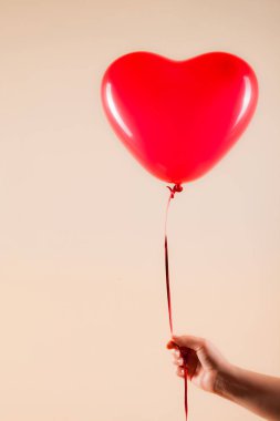 Kadın eli kırmızı kauçuk, şişme kalp şeklinde balon tutuyor. Aşk, ilişki, sevgililer günü ve doğum günü kutlaması konsepti. Stüdyo görüntüsü boş kopya alanı olan bulanık bir arkaplan üzerinde