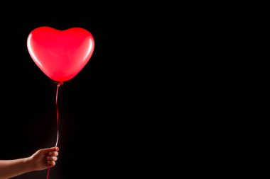 Kadın eli kırmızı kauçuk, şişme kalp şeklinde balon tutuyor. Aşk, ilişki, sevgililer günü ve doğum günü kutlaması konsepti. Stüdyo görüntüsü boş kopya alanı olan bulanık bir arkaplan üzerinde
