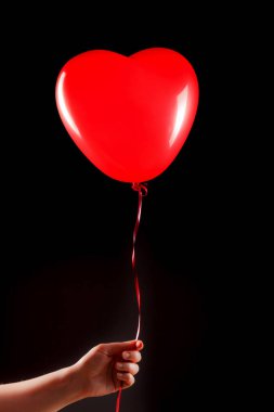 Kadın eli kırmızı kauçuk, şişme kalp şeklinde balon tutuyor. Aşk, ilişki, sevgililer günü ve doğum günü kutlaması konsepti. Stüdyo görüntüsü boş kopya alanı olan bulanık bir arkaplan üzerinde