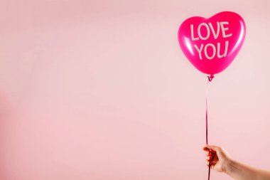 Kadın eli kırmızı kauçuk, şişme kalp şeklinde balon tutuyor. Aşk, ilişki, sevgililer günü ve doğum günü kutlaması konsepti. Stüdyo görüntüsü boş kopya alanı olan bulanık bir arkaplan üzerinde