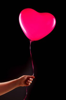 Kadın eli kırmızı kauçuk, şişme kalp şeklinde balon tutuyor. Aşk, ilişki, sevgililer günü ve doğum günü kutlaması konsepti. Stüdyo görüntüsü boş kopya alanı olan bulanık bir arkaplan üzerinde