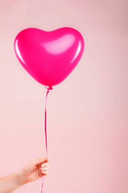 Kadın eli kırmızı kauçuk, şişme kalp şeklinde balon tutuyor. Aşk, ilişki, sevgililer günü ve doğum günü kutlaması konsepti. Stüdyo görüntüsü boş kopya alanı olan bulanık bir arkaplan üzerinde