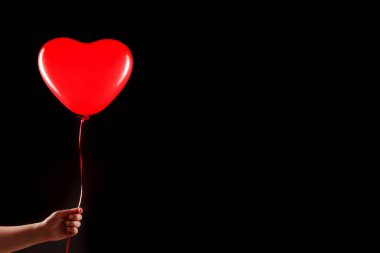 Kadın eli kırmızı kauçuk, şişme kalp şeklinde balon tutuyor. Aşk, ilişki, sevgililer günü ve doğum günü kutlaması konsepti. Stüdyo görüntüsü boş kopya alanı olan bulanık bir arkaplan üzerinde