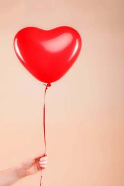 Kadın eli kırmızı kauçuk, şişme kalp şeklinde balon tutuyor. Aşk, ilişki, sevgililer günü ve doğum günü kutlaması konsepti. Stüdyo görüntüsü boş kopya alanı olan bulanık bir arkaplan üzerinde