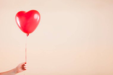Kadın eli kırmızı kauçuk, şişme kalp şeklinde balon tutuyor. Aşk, ilişki, sevgililer günü ve doğum günü kutlaması konsepti. Stüdyo görüntüsü boş kopya alanı olan bulanık bir arkaplan üzerinde