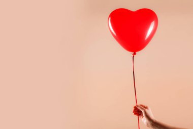 Kadın eli kırmızı kauçuk, şişme kalp şeklinde balon tutuyor. Aşk, ilişki, sevgililer günü ve doğum günü kutlaması konsepti. Stüdyo görüntüsü boş kopya alanı olan bulanık bir arkaplan üzerinde