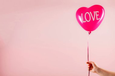 Kadın eli kırmızı kauçuk, şişme kalp şeklinde balon tutuyor. Aşk, ilişki, sevgililer günü ve doğum günü kutlaması konsepti. Stüdyo görüntüsü boş kopya alanı olan bulanık bir arkaplan üzerinde