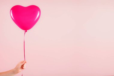Kadın eli kırmızı kauçuk, şişme kalp şeklinde balon tutuyor. Aşk, ilişki, sevgililer günü ve doğum günü kutlaması konsepti. Stüdyo görüntüsü boş kopya alanı olan bulanık bir arkaplan üzerinde