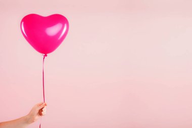 Kadın eli kırmızı kauçuk, şişme kalp şeklinde balon tutuyor. Aşk, ilişki, sevgililer günü ve doğum günü kutlaması konsepti. Stüdyo görüntüsü boş kopya alanı olan bulanık bir arkaplan üzerinde