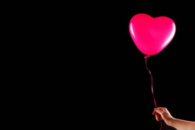 Kadın eli kırmızı kauçuk, şişme kalp şeklinde balon tutuyor. Aşk, ilişki, sevgililer günü ve doğum günü kutlaması konsepti. Stüdyo görüntüsü boş kopya alanı olan bulanık bir arkaplan üzerinde