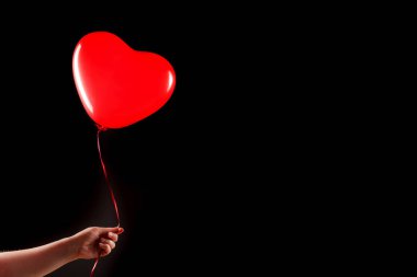 Kadın eli kırmızı kauçuk, şişme kalp şeklinde balon tutuyor. Aşk, ilişki, sevgililer günü ve doğum günü kutlaması konsepti. Stüdyo görüntüsü boş kopya alanı olan bulanık bir arkaplan üzerinde