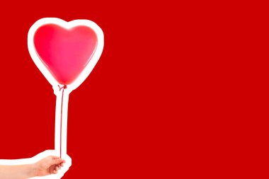Kadın eli kırmızı kauçuk, şişme kalp şeklinde balon tutuyor. Aşk, ilişki, sevgililer günü ve doğum günü kutlaması konsepti. Boş kopya alanı olan dergi tarzı moda kolajı