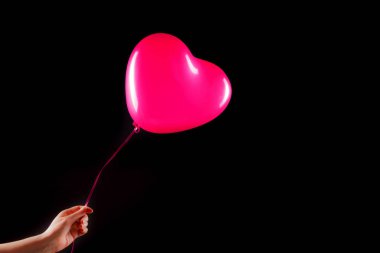 Kadın eli kırmızı kauçuk, şişme kalp şeklinde balon tutuyor. Aşk, ilişki, sevgililer günü ve doğum günü kutlaması konsepti. Stüdyo görüntüsü boş kopya alanı olan bulanık bir arkaplan üzerinde