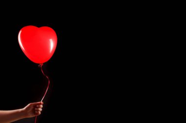 Kadın eli kırmızı kauçuk, şişme kalp şeklinde balon tutuyor. Aşk, ilişki, sevgililer günü ve doğum günü kutlaması konsepti. Stüdyo görüntüsü boş kopya alanı olan bulanık bir arkaplan üzerinde