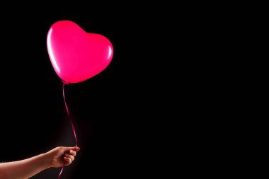 Kadın eli kırmızı kauçuk, şişme kalp şeklinde balon tutuyor. Aşk, ilişki, sevgililer günü ve doğum günü kutlaması konsepti. Stüdyo görüntüsü boş kopya alanı olan bulanık bir arkaplan üzerinde