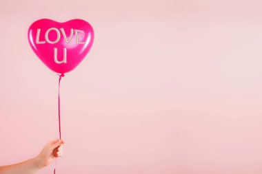 Kadın eli kırmızı kauçuk, şişme kalp şeklinde balon tutuyor. Aşk, ilişki, sevgililer günü ve doğum günü kutlaması konsepti. Stüdyo görüntüsü boş kopya alanı olan bulanık bir arkaplan üzerinde