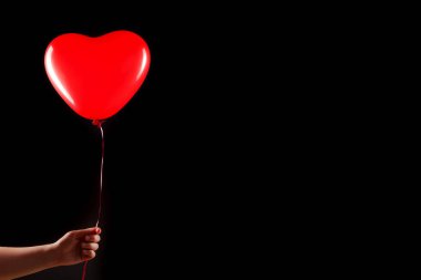 Kadın eli kırmızı kauçuk, şişme kalp şeklinde balon tutuyor. Aşk, ilişki, sevgililer günü ve doğum günü kutlaması konsepti. Stüdyo görüntüsü boş kopya alanı olan bulanık bir arkaplan üzerinde