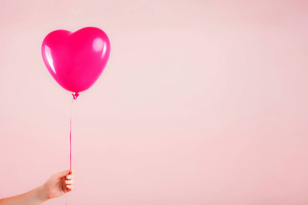 Женская рука держит розовый резиновый надувной шарик в форме сердца. Любовь, отношения, день святого Валентина и празднование дня рождения. Снимок студии на абстрактном размытом фоне с пустым местом для копирования
