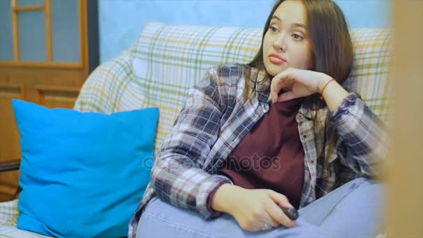 Mujer joven con el pelo largo sentado en el sofá y viendo la televisión . — Vídeos de Stock