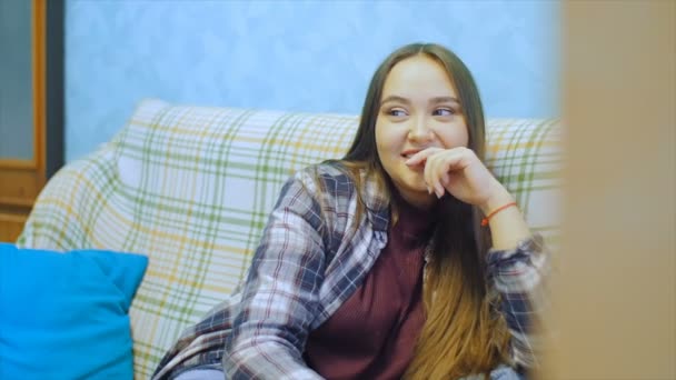 Mujer joven con el pelo largo sentado en el sofá y viendo la televisión . — Vídeos de Stock