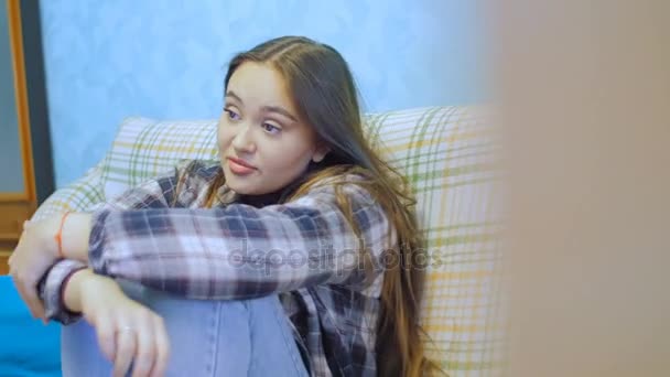 Mujer joven con el pelo largo sentado en el sofá y viendo la televisión . — Vídeos de Stock