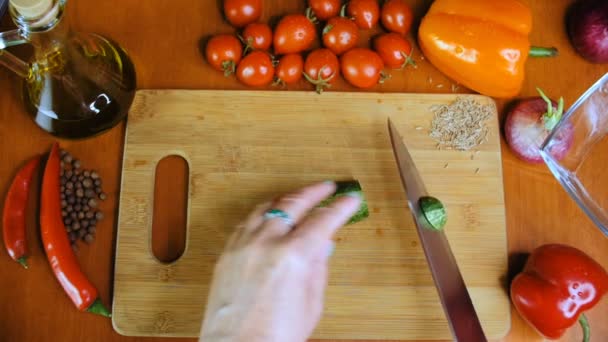 Een vrouw is het snijden van een komkommer op de keukentafel. — Stockvideo