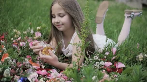 La fille se trouve dans l'herbe et regarde les flacons de parfum . — Video