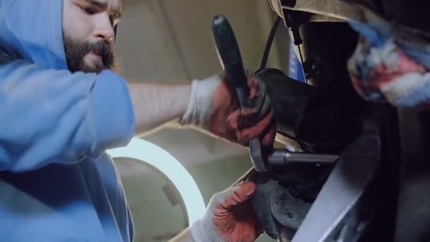 A bearded car mechanic tightens the bolts on the engine of the machine with the tool. — Stock Video