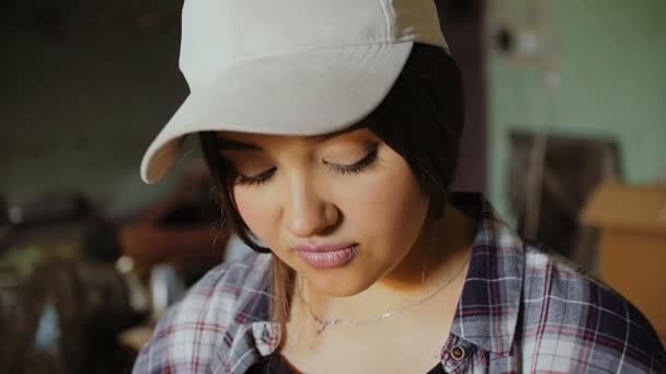 Hermosa chica en una gorra de béisbol blanca se para en el garaje y mira a la cámara . — Vídeo de stock